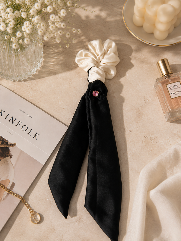 Gala ivory silk scrunchie with black ribbon tails and pink crystal — flat lay